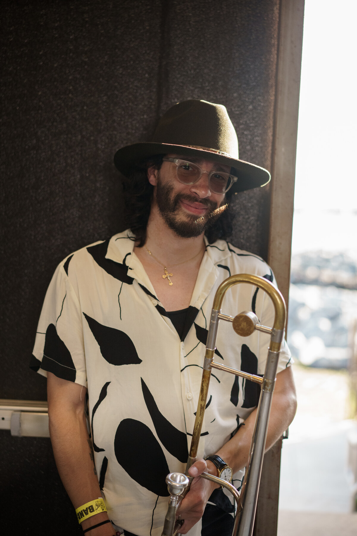 Andrew Morales smiling by a window, holding his trombone