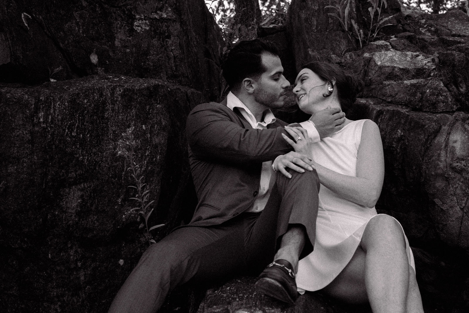 Evan leaning toward Gabrielle as she smiles, seated among rocks in a black-and-white portrait
