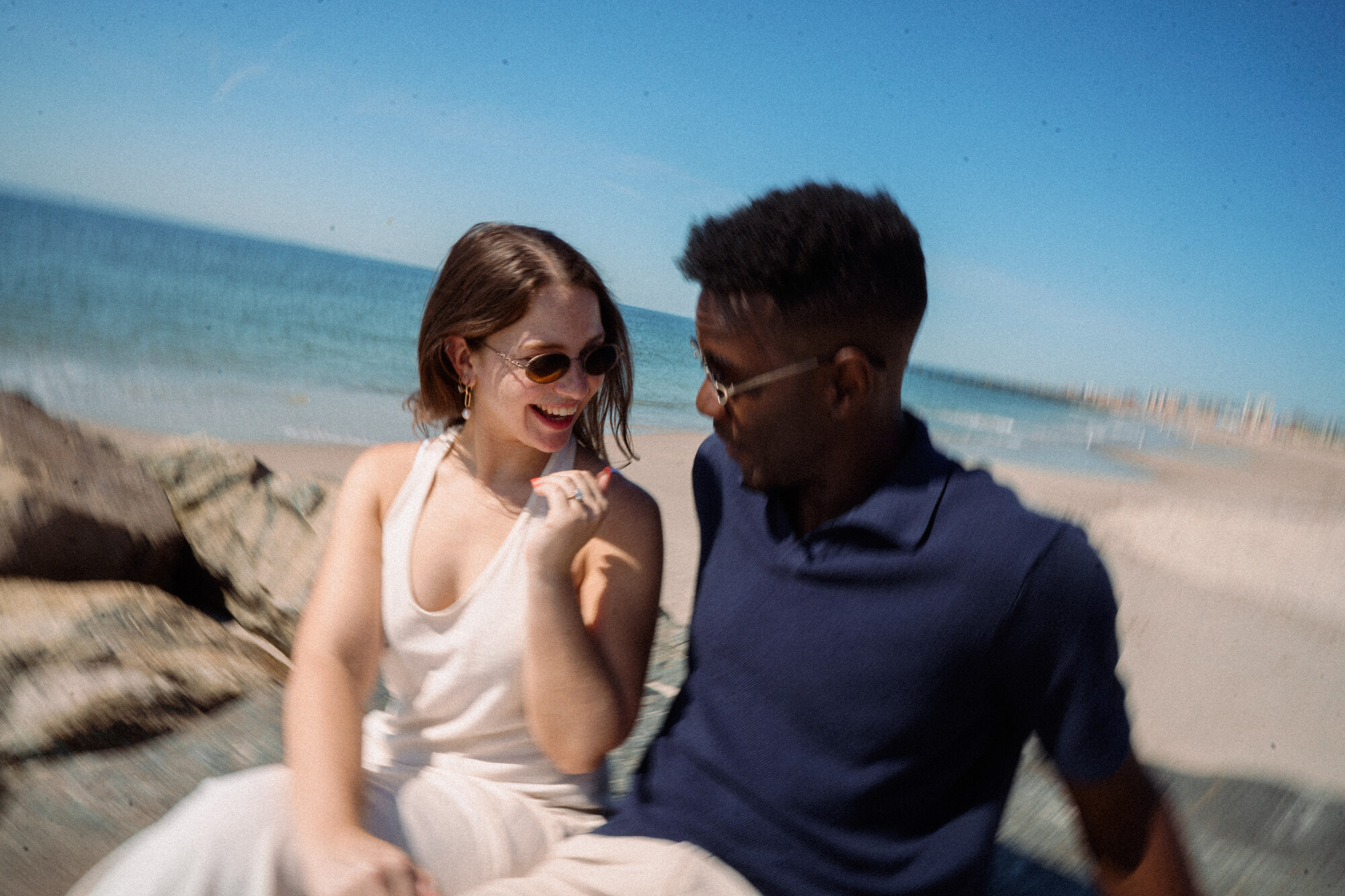 Ify and Ashley laughing together by the ocean, Ashley lifting her hand to show her ring
