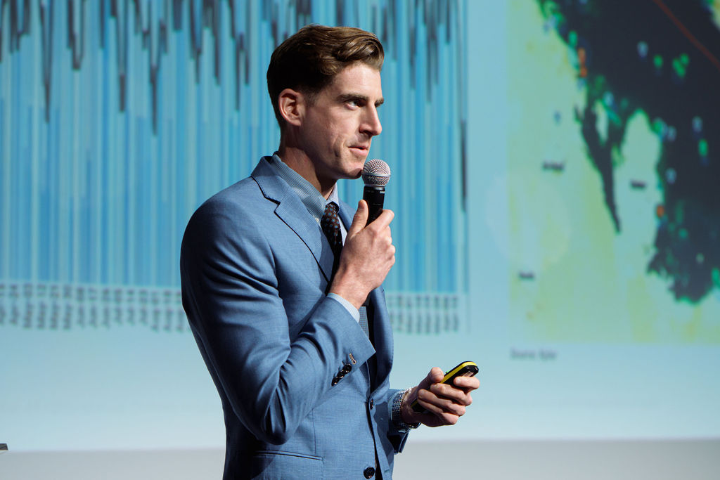 Kpler Insights speaker holding a microphone in front of a blue-lit presentation