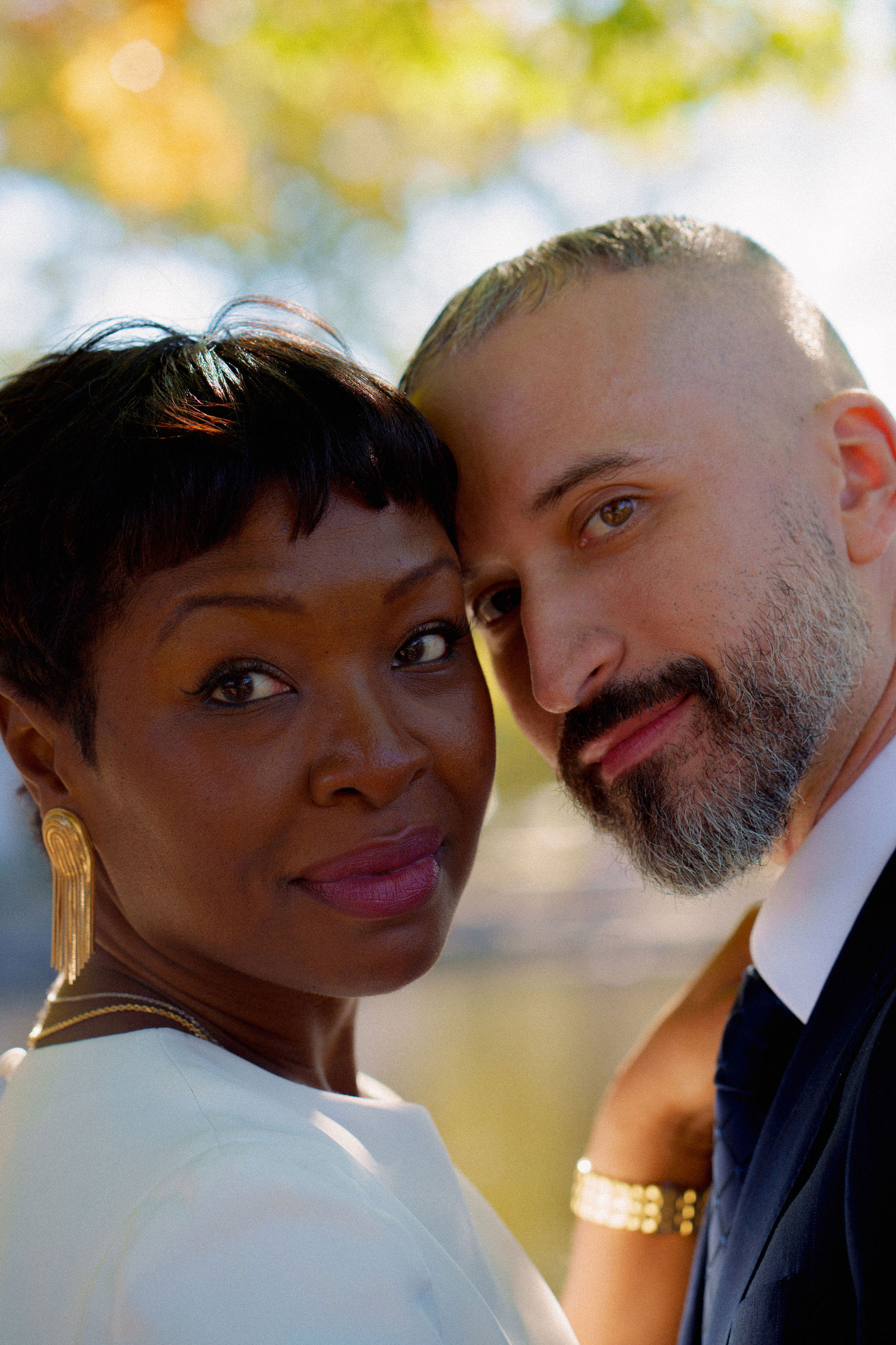 Noe and John leaning their heads together in a sunlit wedding portrait