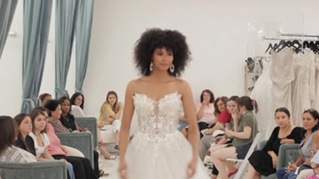 A model in a bridal gown walking between guests at the Bridal Reflections Carle Place opening